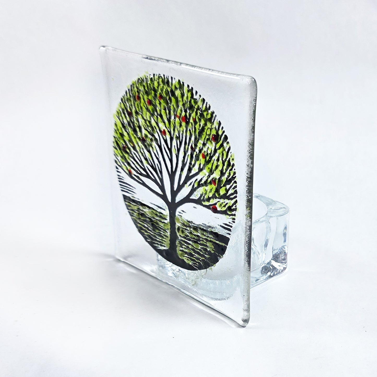 Handmade fused glass tealight holder featuring a green tree design with red accents. A beautiful nature-inspired glass gift for the home.